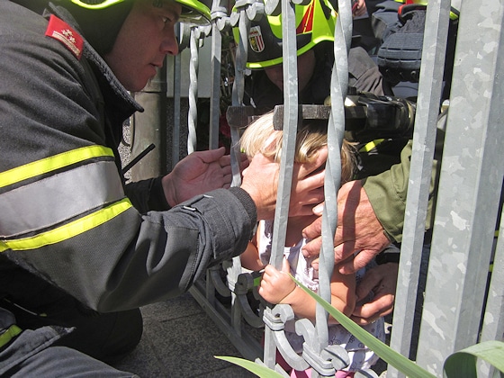 Ein Kind steckt im Zaun fest. Behutsam retten Feuerwehrleute das Mädchen. Foto: Kollinger