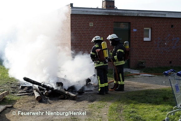 Nienburger Feuerwehrleute löschen einen Holzstapel, der direkt neben einem Gebäude angezündet worden war. Foto: Feuerwehr Nienburg/Henkel