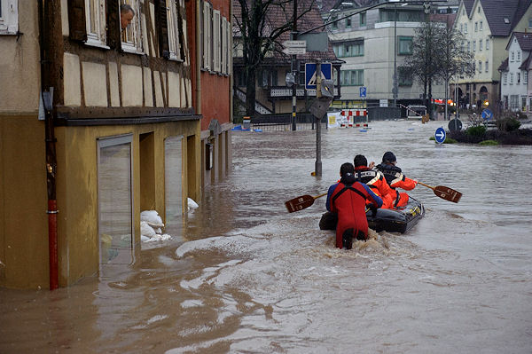 DLRG-Helfer fahren mit einem Schlauchboot auf einer Straße in Backnang, um eingeschlossene Gäste eines Hotels zu befreien. Ein Anwohner beobachtet die Szene aus dem Fenster. Foto: Oskar Eyb