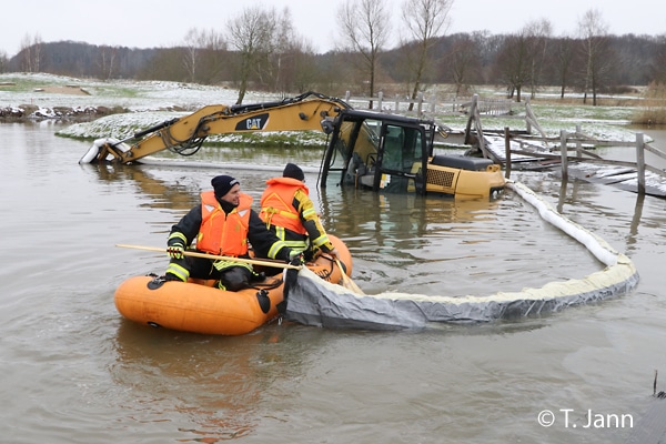 Feuerwehrleute legen mittels Schlauchboot eine Ölsperre um einen Bagger. Diesen hatten Unbekannte gestohlen und in einem See versenkt.