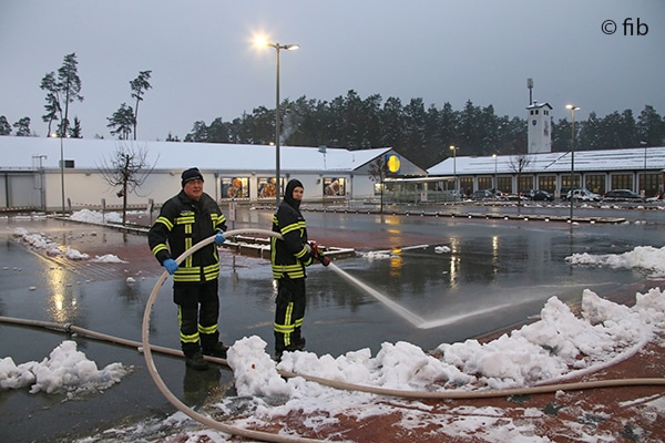 Feuerwehrleute mit Schlauch und Strahlrohr auf einem teilweise verschneiten Parkplatz