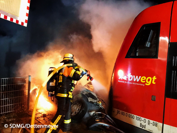 Ein Feuerwehrmann löscht einen brennenden Pkw, der von einem Zug erfasst worden ist.