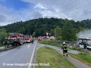 Feuerwehrmänner löschen einen brennenden Bus, der in der Nähe von Blaustein auf einem Bahnübergang mit einem Zug kollidiert ist.