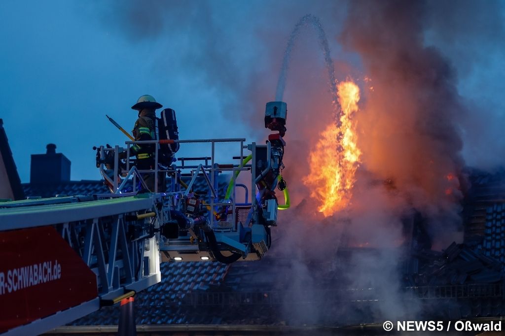 Einsatzkräfte der Feuerwehr bekämpfen mit einem Hubrettungsfahrzeug die Flammen im Dachstuhl