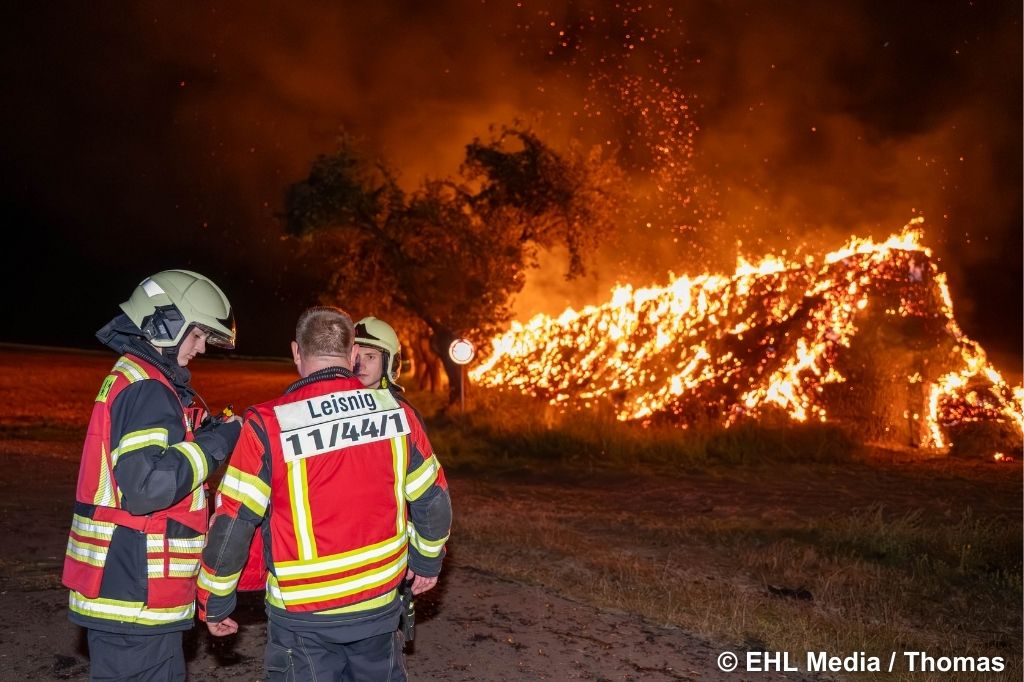 Strohballen in Flammen; im Vordergrund Feuerwehr