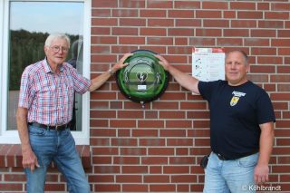 Ortsbrandmeister Matthias Eul (rechts) und der Vorsitzende des Fördervereins der FF Iddensen, Hans-Joachim Ehrhorn mit AED