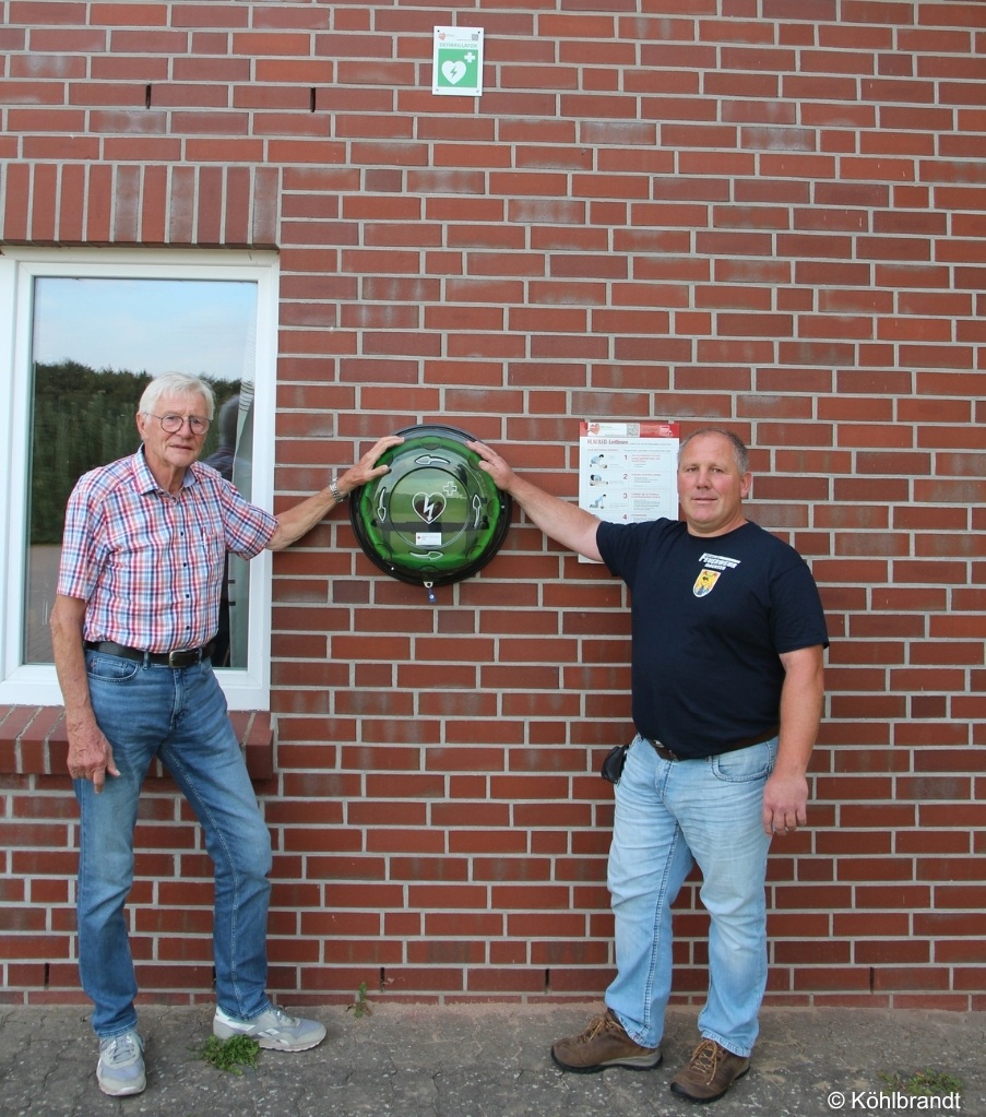 Ortsbrandmeister Matthias Eul (rechts) und der Vorsitzende des Fördervereins der FF Iddensen, Hans-Joachim Ehrhorn mit AED