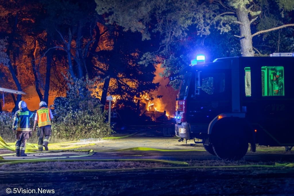 Einsatzkräfte der Feuerwehr im Bereich der Reitanlage in Heusenstamm. Im Hintergrund ist deutlicher Feuerschein hinter dem Baumbestand zu erkennen.