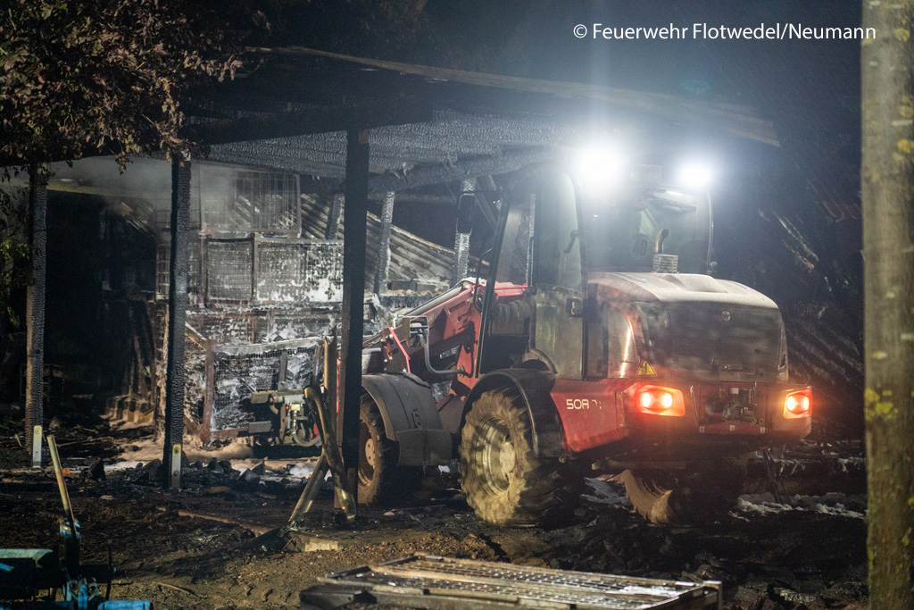 Mit einem Teleskoplader holen die Kräfte Material aus dem Unterstand, um es in sicherer Distanz vollends abzulöschen. Foto: Feuerwehr Flotwedel/Neumann
