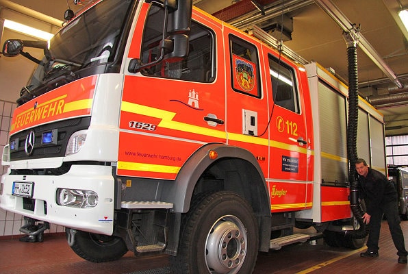 Abgasabsauganlage bei der Feuerwehr Hamburg - auch ein Teil des Arbeitsschutzes. Carsten Behncken, Zugführer an F 26 in Hamburg-Bergedorf, zeigt einen neuartigen Absaugschlauch für die Auspuffanlage des Hilfeleistungs-Löschgruppenfahrzeugs. Statt lose von der Decke baumelnd, was Unfälle begünstigt, hängt der Schlauch jetzt per Magnet dicht am Fahrzeug.Foto: Timo Jann