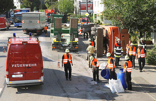 Baggerunfall in München: die Baumaschine ist von einem Tieflader gestürzt, die Feuerwehr streut ausgelaufenes Öl ab. Foto: BF München
